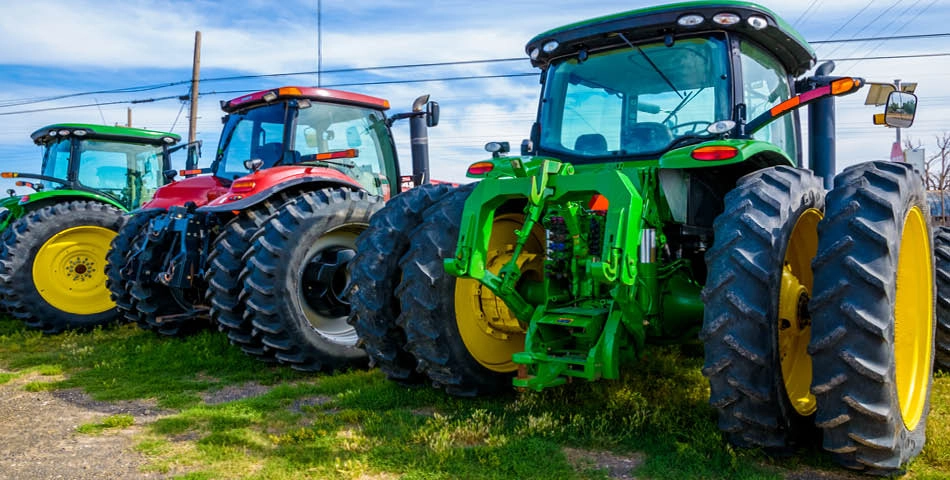 Three large modern tractors, colored green, red, and blue, are parked side by side on grass under a partly cloudy sky.