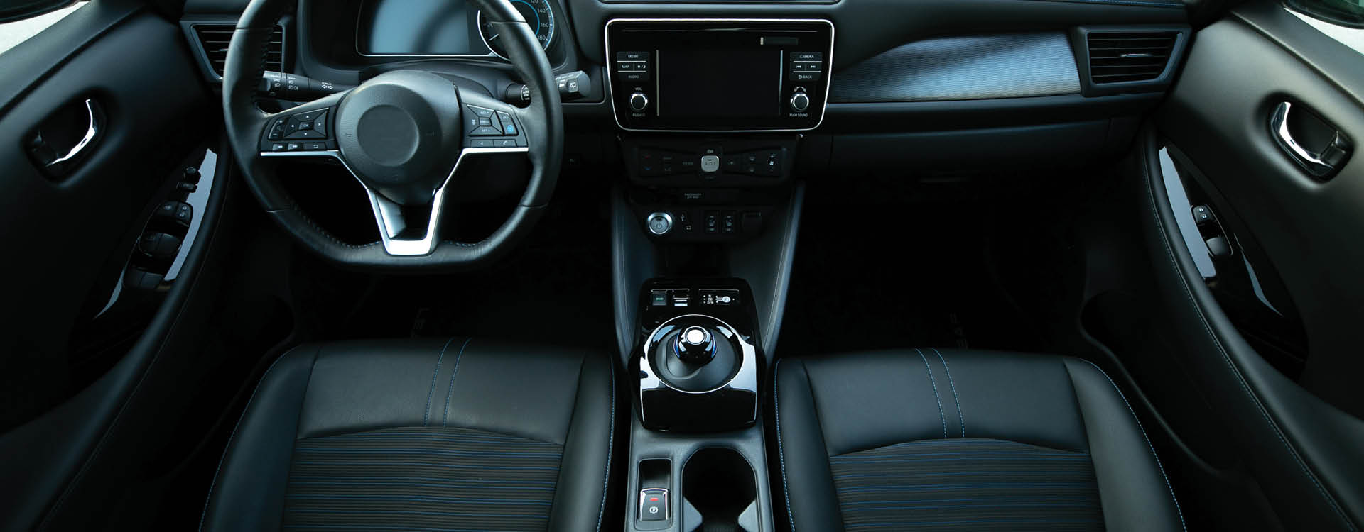 View of a modern car interior featuring a steering wheel, central touchscreen display, gear selector, cup holders, and black leather seats.