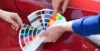 Two people compare paint color swatches to the exterior of a red car.