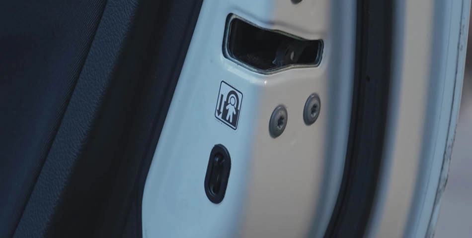 Close-up of a car door's child lock mechanism with a sticker showing a child lock icon and a switch below it.