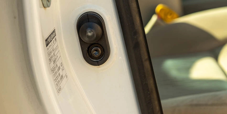 Close-up of a car door jamb showing a door sensor or pin switch and a manufacturer information sticker, with part of the car interior visible in the background.