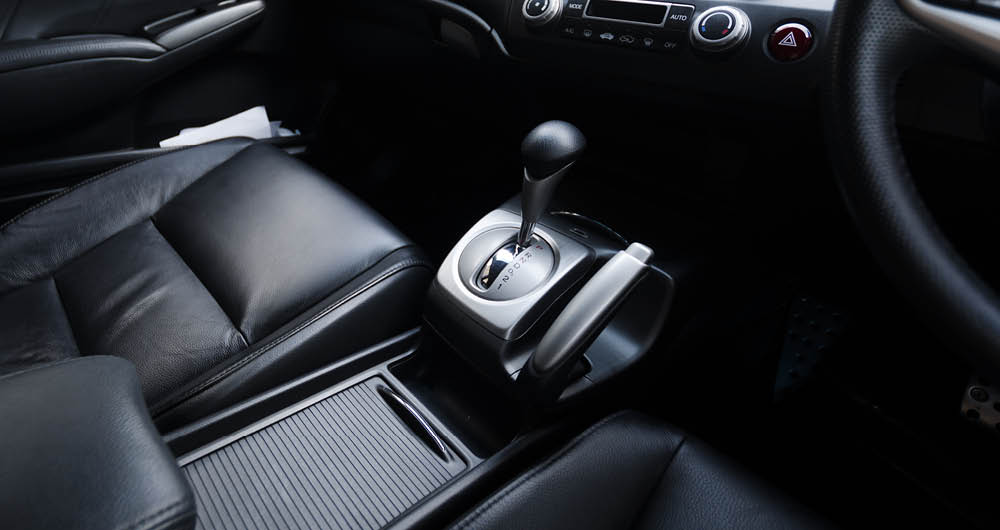 Close-up view of a car's automatic gear shift lever and black leather seats in the front interior.