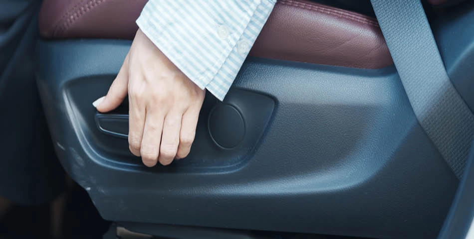 A person adjusts a car seat using a lever located on the side of the seat.