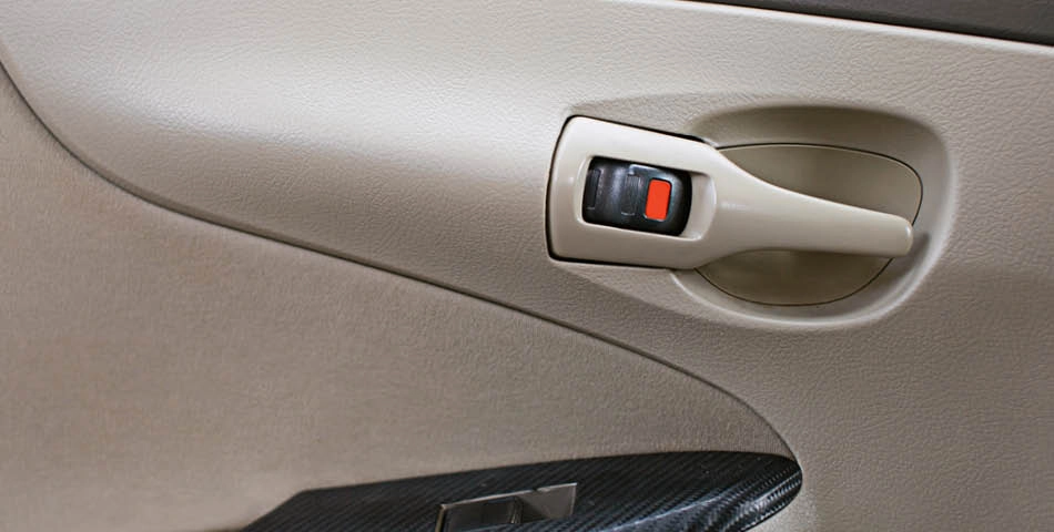 Close-up of a beige car interior door handle with a black and red lock switch.
