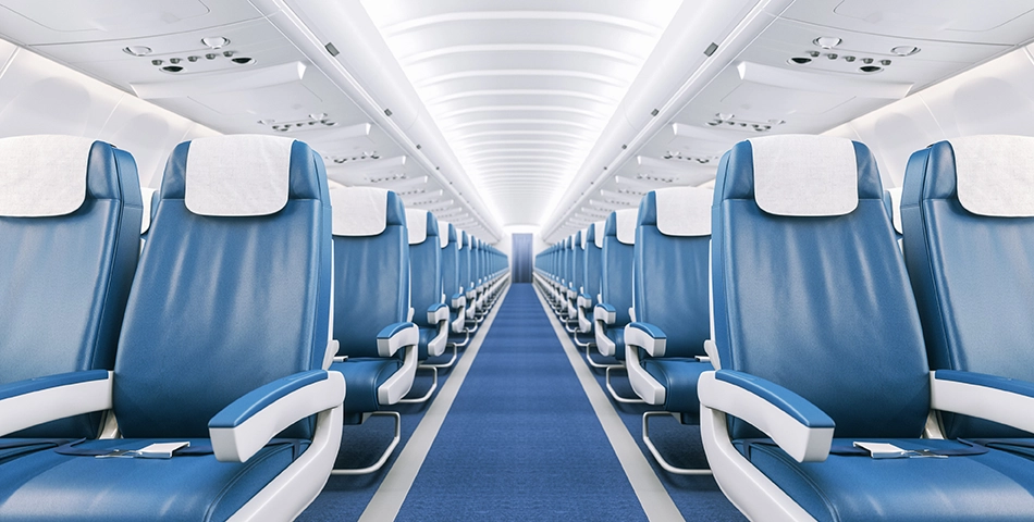 Interior of a commercial airplane showing rows of empty blue seats with white headrest covers, a blue carpeted aisle, and overhead storage compartments.