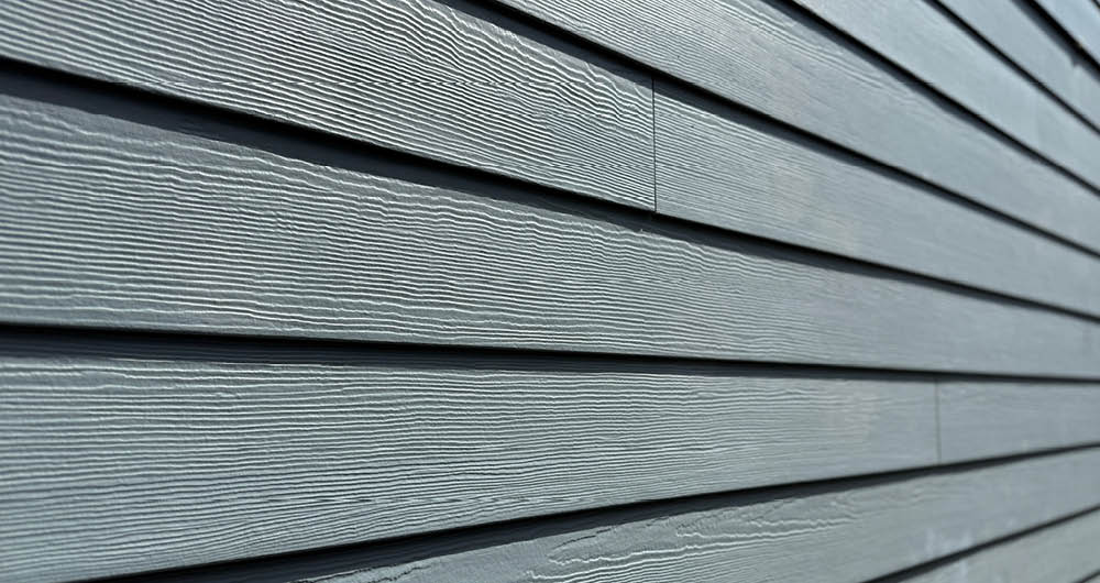 Close-up view of horizontal gray fiber cement siding panels with a wood grain texture on a building exterior.