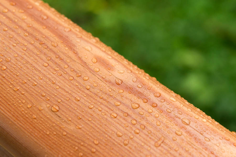Close-up of water droplets on a wooden surface with a blurred green background.
