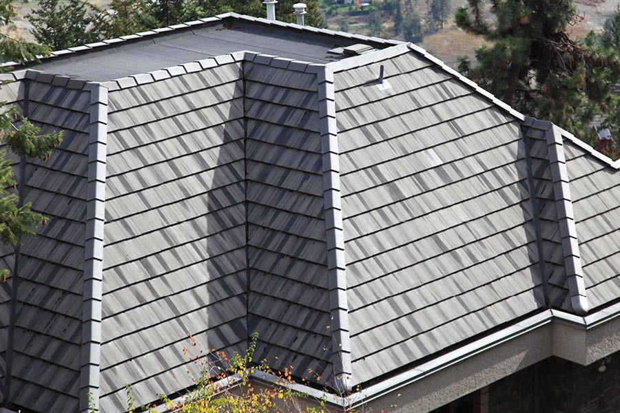 Gray metal shingle roof with multiple hips and slopes, surrounded by trees.
