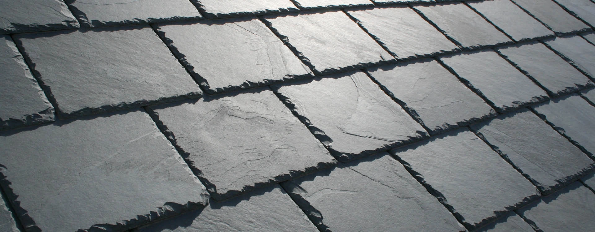 Close-up view of overlapping gray slate roof tiles arranged in rows, showing texture and irregular edges.