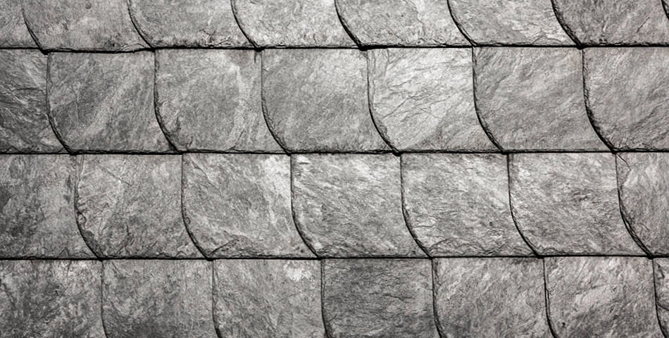 Close-up view of overlapping gray slate roof tiles arranged in a regular, repeating pattern.