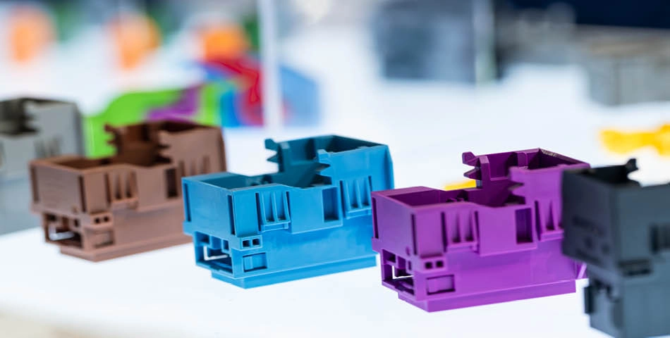 Several colorful plastic components are displayed in a row on a white surface, including blue, purple, and brown pieces, with a blurred background.