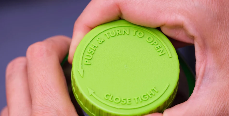 A close-up of hands gripping a green child-resistant bottle cap labeled "PUSH & TURN TO OPEN" and "CLOSE TIGHT" with directional arrows.