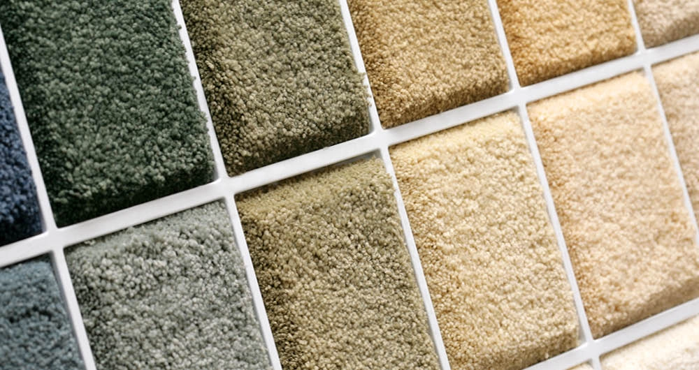 Close-up of a display featuring square carpet samples in various earth tone shades, including greens, browns, and beiges, arranged in a grid pattern.