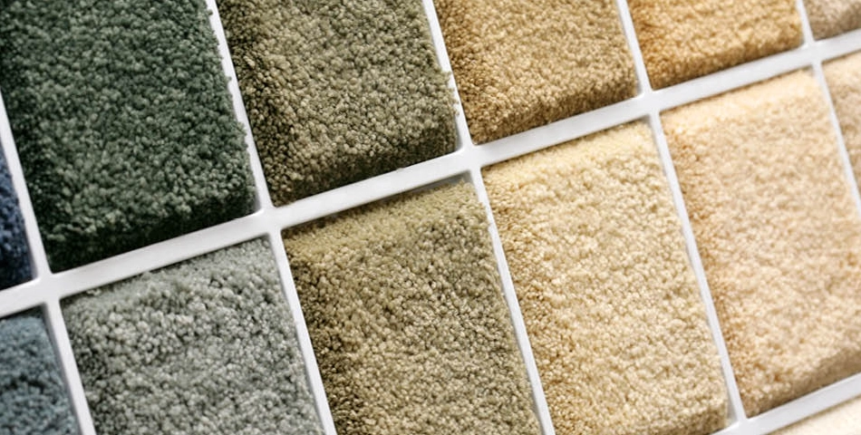 Close-up of a display board showing various carpet samples in shades of green, beige, and yellow, arranged in a grid pattern.