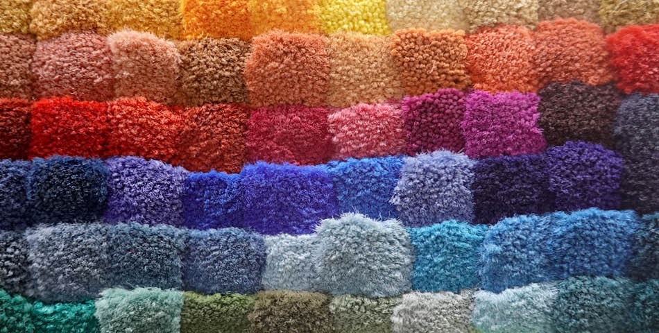 Rows of small, square carpet or fabric samples in various colors ranging from reds and oranges to blues, purples, and greens, arranged in a gradient pattern.