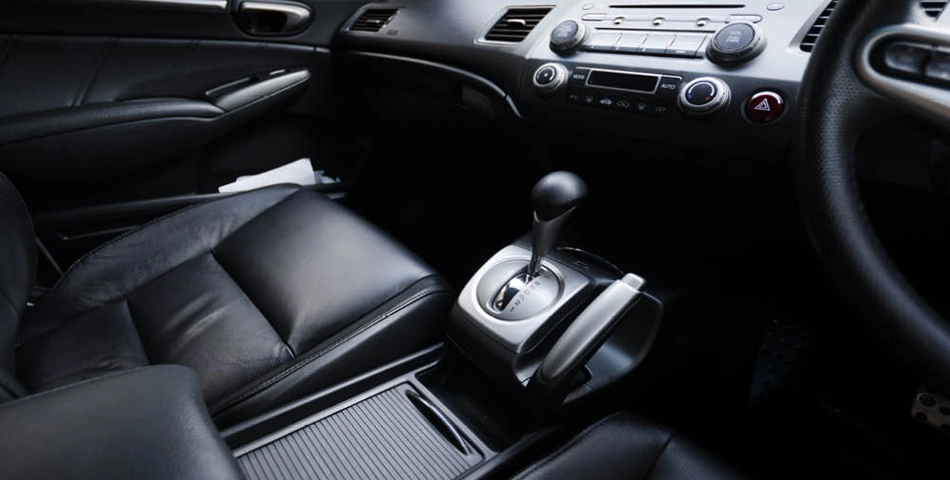 Interior of a car showing black leather seats, a gear shift lever, dashboard controls, and part of the steering wheel on the right side.