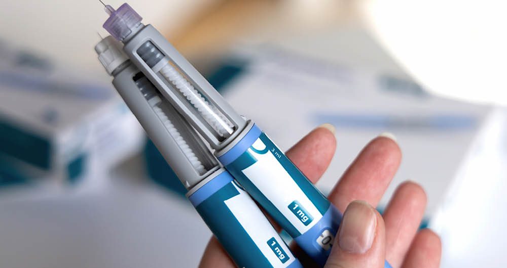 A hand holding two insulin pens with needles attached, used for administering medication.