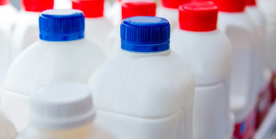 Plastic milk bottles with blue, red, and white caps are arranged closely together, viewed from above and at an angle.