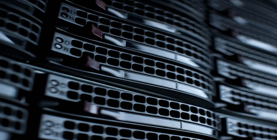 Close-up view of stacked server racks with black vented panels and indicator lights, showing a section of a data center or server room.