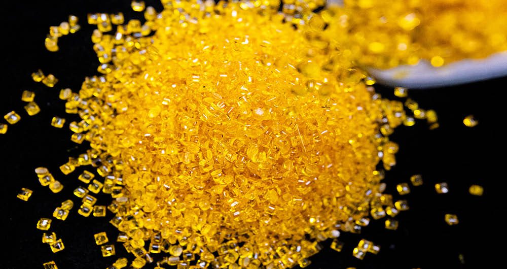 A close-up of a pile of small, yellow plastic pellets scattered on a black surface.