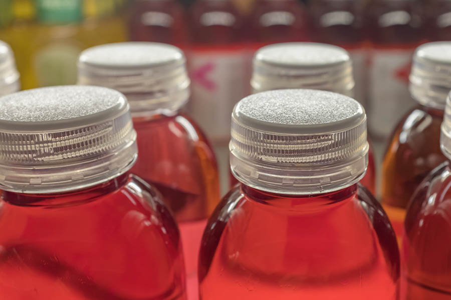 Close-up of several plastic bottles filled with a reddish-brown liquid, each sealed with a clear plastic cap, arranged in rows.