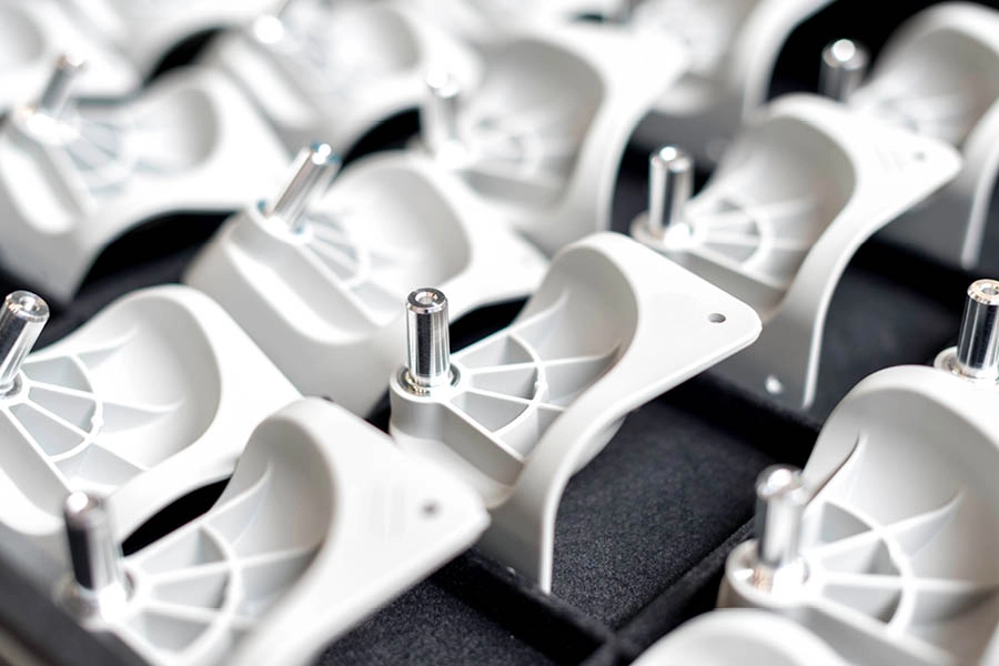 A close-up view of multiple identical white plastic components with metal pins, arranged in an organized grid pattern.