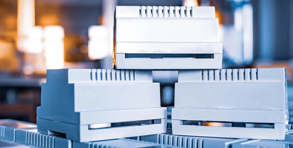 Stacked white DIN rail enclosures for electrical components are shown in a manufacturing or industrial setting.