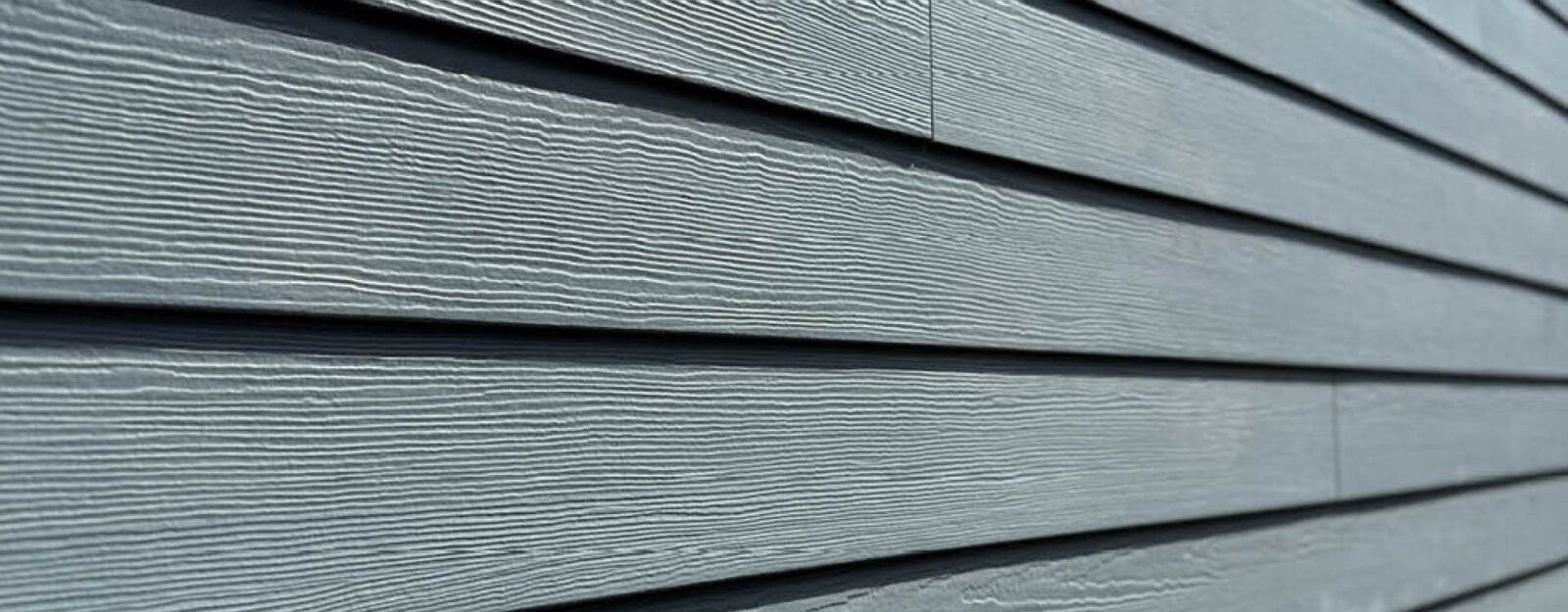 Close-up view of grey horizontal siding panels on a building exterior, showing wood grain texture and overlapping edges.