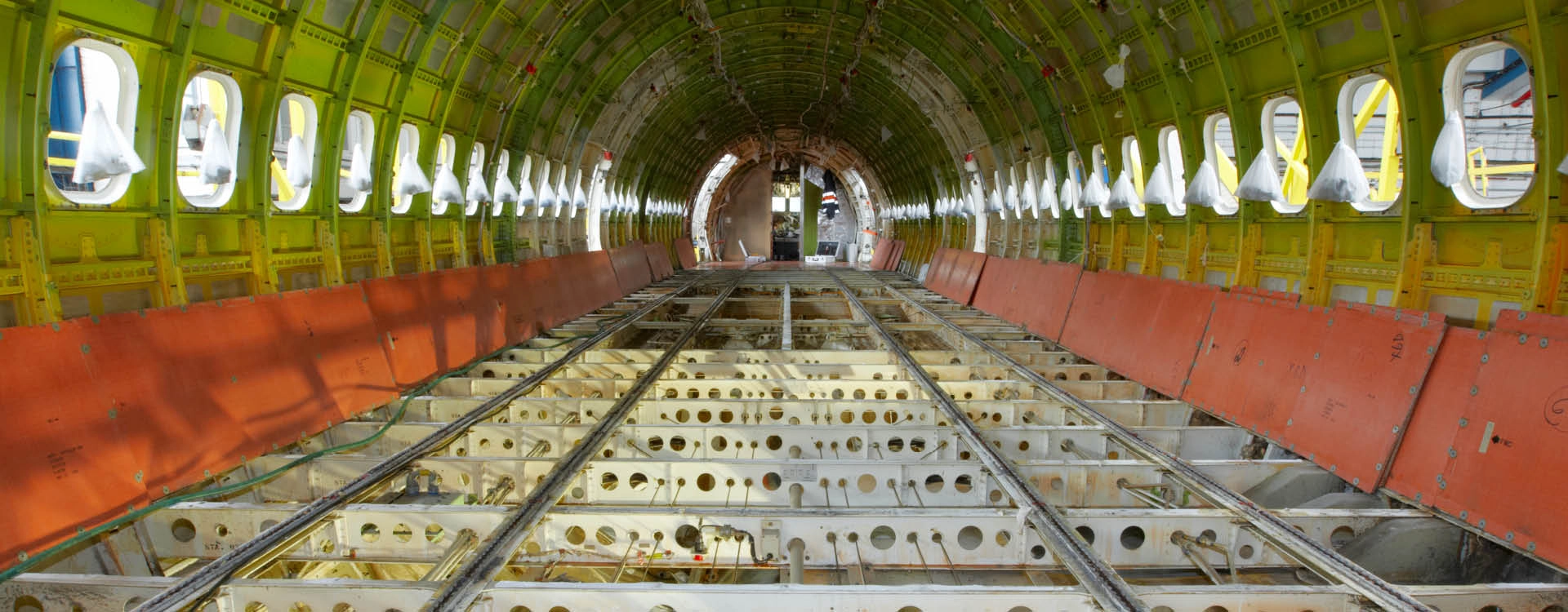 Interior view of an empty airplane fuselage, showing exposed metal framework, window cutouts along both sides, and no flooring or seats installed.
