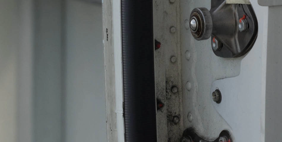 Close-up view of a section of metal machinery with screws, bolts, and a black cable or hose running vertically.