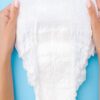 Close-up of hands holding a white disposable diaper against a light blue background.