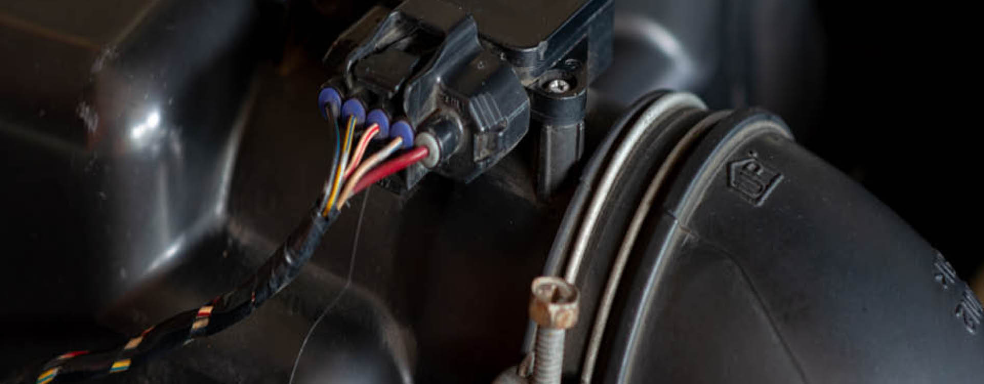 Close-up view of an automotive engine component with several colored wires connected to a black plastic sensor or connector.