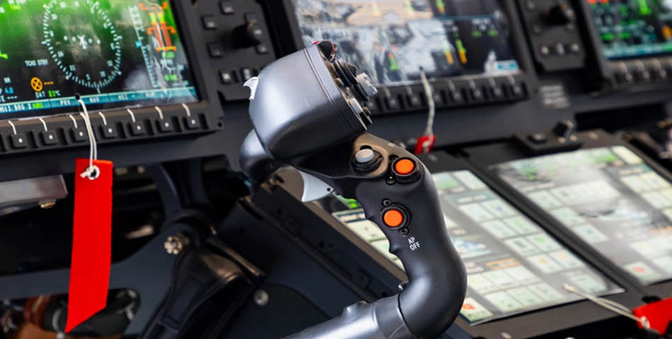 Close-up of a modern aircraft cockpit showing flight controls, digital displays, and labeled control switches with red tags.