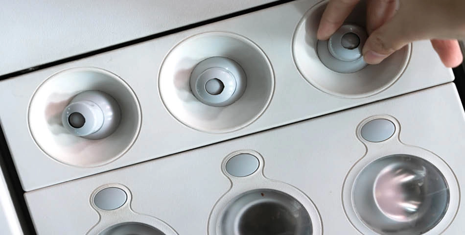 A hand is placing a plastic cup lid into a circular dispenser slot on a white beverage station.