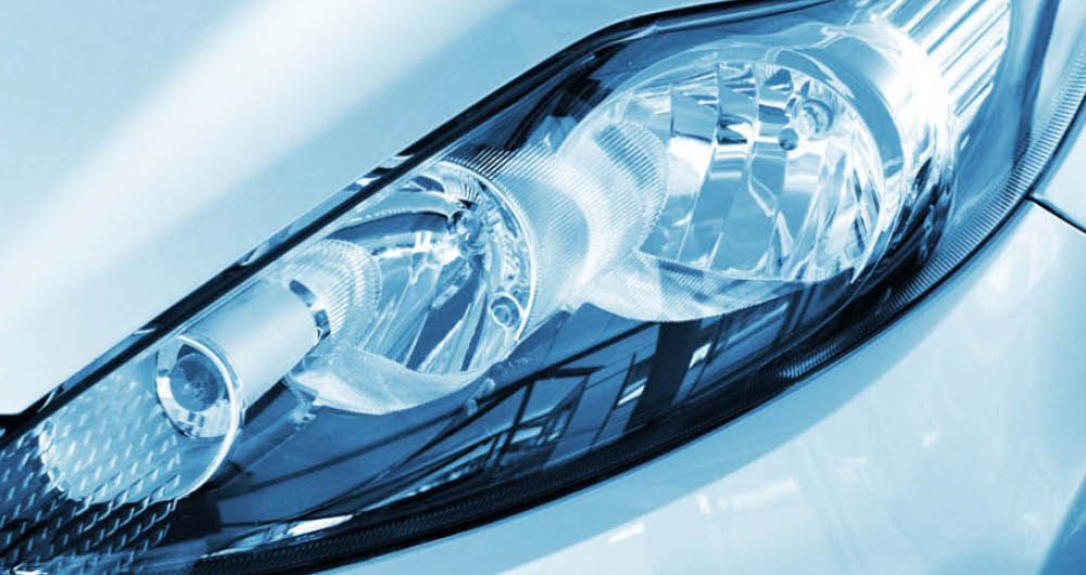 Close-up of a modern car's headlight and surrounding blue-tinted bodywork, showing detailed design elements and light reflections.