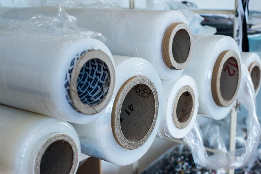Several large rolls of clear plastic film are stacked on a metal rack, with cardboard cores visible at the center of each roll.