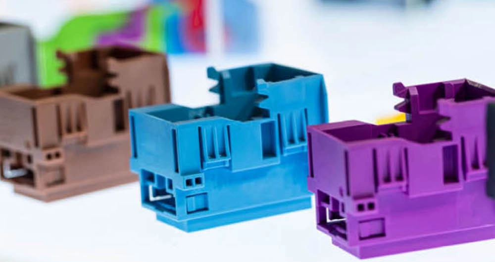 Close-up of three plastic electronic housing components in brown, blue, and purple, arranged in a row on a white surface.