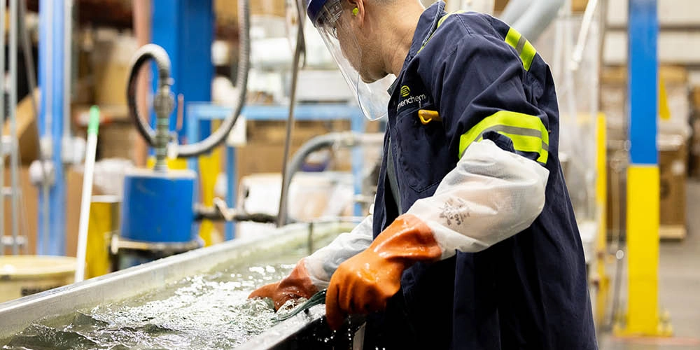 A worker in protective gear and gloves handles materials in a water tank at an industrial facility.