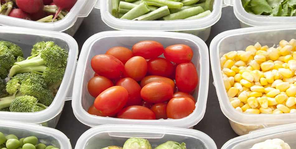 Plastic containers filled with fresh vegetables, including cherry tomatoes, broccoli, corn, green beans, radishes, and leafy greens, arranged in a grid pattern.