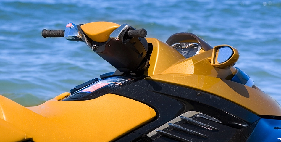 Close-up view of the handlebars and console of a yellow jet ski floating on the water with the ocean in the background.
