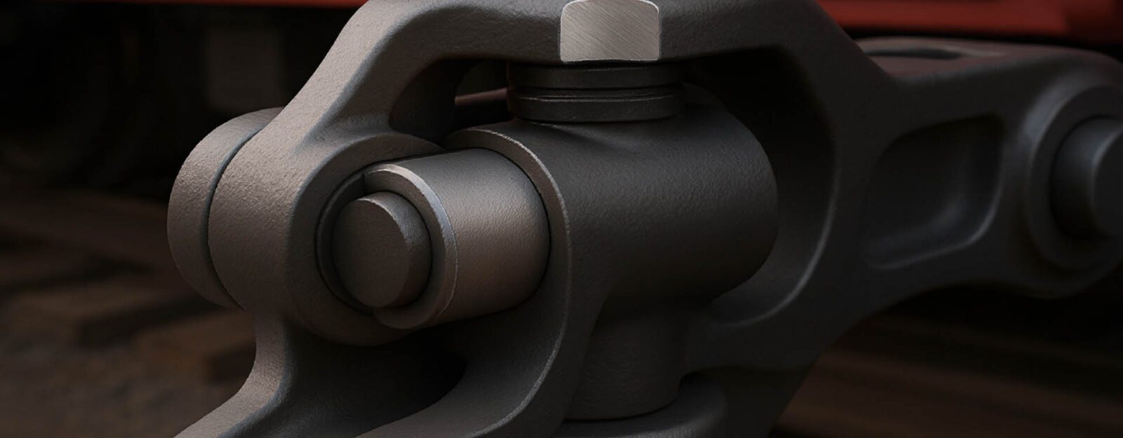 Close-up view of a metal mechanical joint, likely part of a train coupling system, with tracks visible in the blurred background.