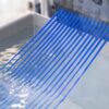Blue plastic filament strands are being extruded from a metal die into a water bath during a manufacturing process.