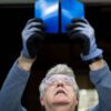 A person wearing safety glasses and gloves holds two blue rectangular objects up to examine them against the light.