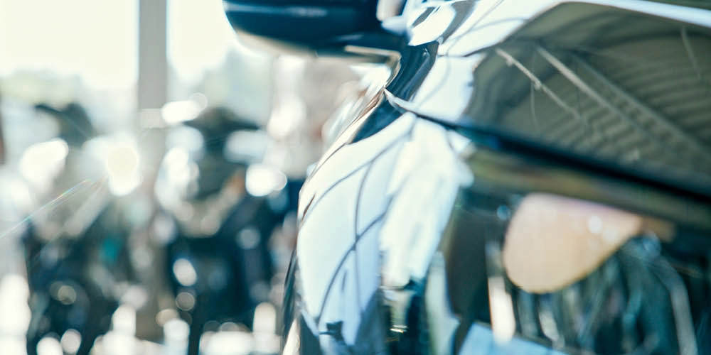 Close-up of the side of a shiny black car with blurred motorcycles and a bright background in a showroom.
