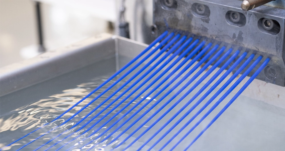 Blue polymer filaments are extruded through a metal die into a water bath during a manufacturing process.