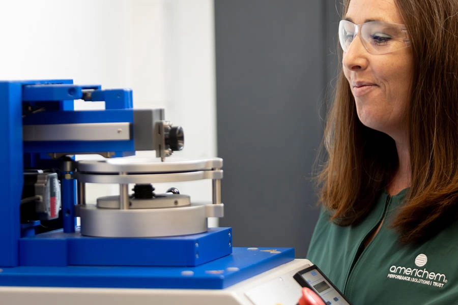 A woman in safety glasses operates a blue laboratory machine at Americhem.