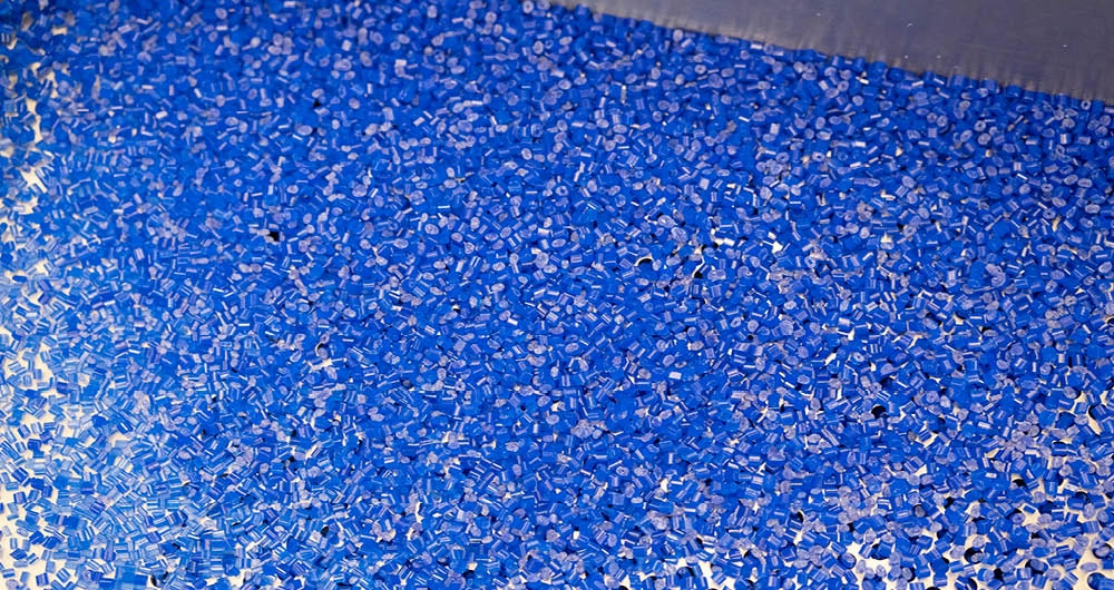 A large quantity of small blue plastic pellets spread across a flat surface, likely in an industrial setting.