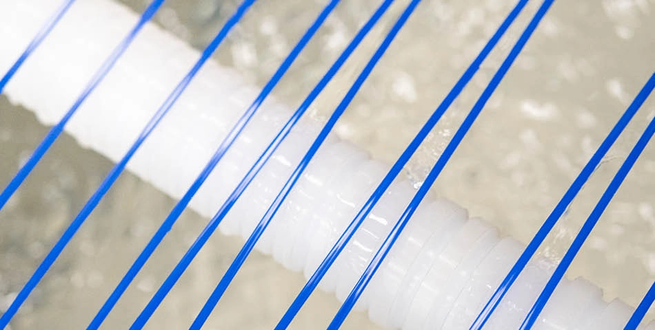 Close-up of blue strings or wires running diagonally across a textured white cylindrical object with a blurred background.