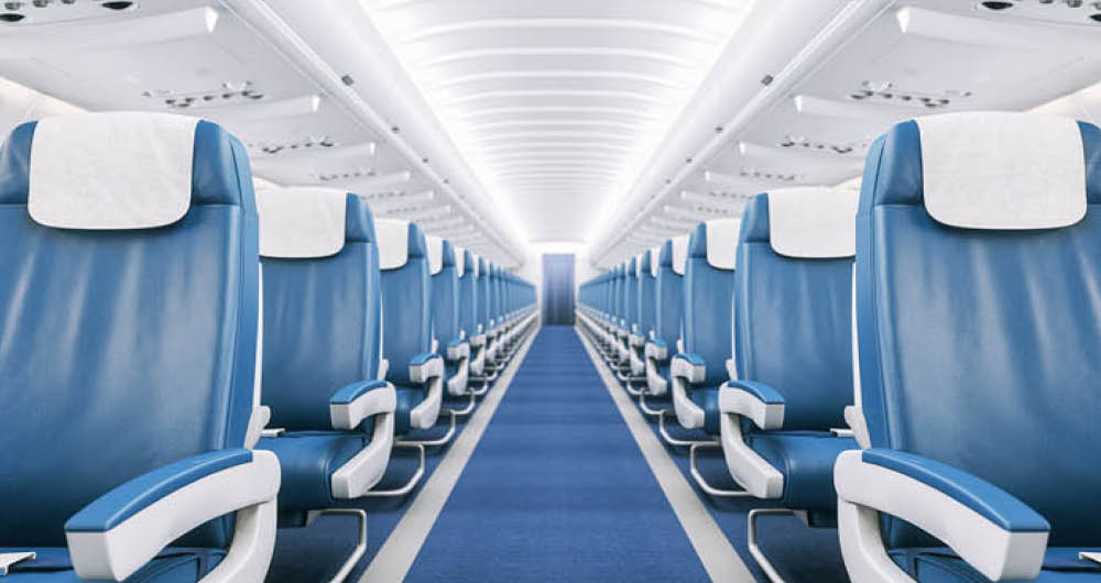 Empty airplane cabin with rows of blue seats, white headrest covers, and a central aisle under bright overhead lighting.