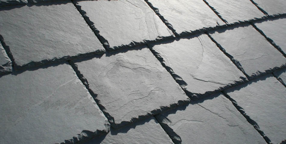 Close-up view of overlapping rectangular gray slate roof tiles arranged in a uniform pattern.